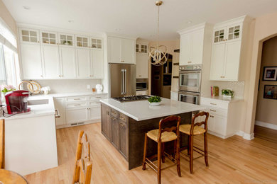 Example of a mid-sized transitional u-shaped medium tone wood floor and brown floor kitchen design in San Francisco with an undermount sink, shaker cabinets, white cabinets, quartz countertops, beige backsplash, ceramic backsplash, stainless steel appliances, an island and white countertops