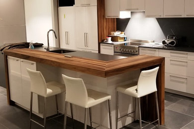 Small minimalist kitchen photo in Montreal with an undermount sink, flat-panel cabinets, gray backsplash, an island, white cabinets, stainless steel appliances and wood countertops