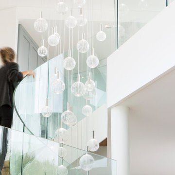 Curved staircase with glass balustrade and pendant cluster, Cornwall
