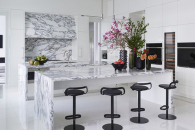 Example of a trendy l-shaped white floor kitchen design in Charlotte with an undermount sink, flat-panel cabinets, white cabinets, gray backsplash, two islands and gray countertops