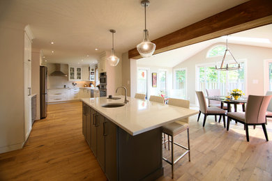 Photo of a large transitional l-shaped eat-in kitchen in Other with shaker cabinets, white cabinets, with island, an undermount sink, stainless steel appliances, medium hardwood floors, brown floor, solid surface benchtops and white splashback.