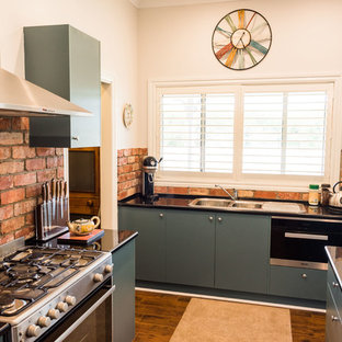 Small farmhouse kitchen pantry inspiration - Example of a small cottage galley linoleum floor and brown floor kitchen pantry design in Geelong with a double-bowl sink, green cabinets, laminate countertops, red backsplash, brick backsplash, stainless steel appliances and an island
