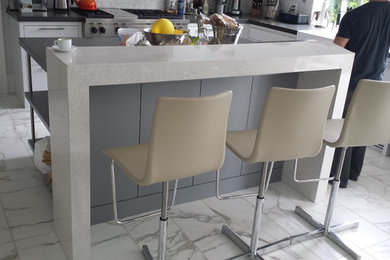 Photo of a large modern l-shaped eat-in kitchen in Toronto with a farmhouse sink, flat-panel cabinets, white cabinets, quartzite benchtops, white splashback, stone tile splashback, stainless steel appliances, marble floors and multiple islands.