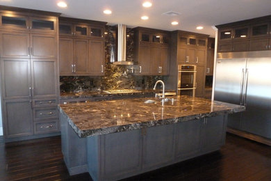 This is an example of a large transitional single-wall separate kitchen in Las Vegas with a double-bowl sink, recessed-panel cabinets, dark wood cabinets, granite benchtops, brown splashback, stone slab splashback, stainless steel appliances, dark hardwood floors, with island, brown floor and brown benchtop.