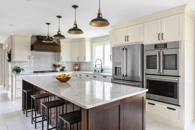 Photo of a large traditional l-shaped eat-in kitchen in Boston with an undermount sink, recessed-panel cabinets, beige cabinets, quartz benchtops, white splashback, ceramic splashback, stainless steel appliances, with island and white benchtop.