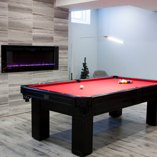 トロントの大きいモダンスタイルのおしゃれな地下室 (全地下、青い壁、ラミネートの床、吊り下げ式暖炉、タイルの暖炉まわり、グレーの床) の写真