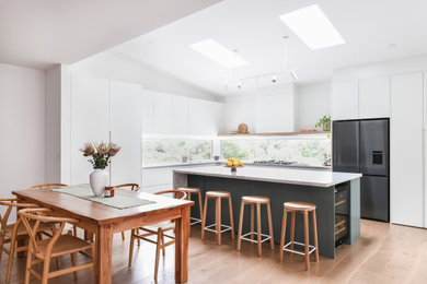 This is an example of a large modern l-shaped open plan kitchen in Sydney with an undermount sink, flat-panel cabinets, green cabinets, quartz benchtops, window splashback, black appliances, medium hardwood floors, with island, brown floor, white benchtop and vaulted.