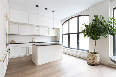 Design ideas for a mid-sized contemporary u-shaped eat-in kitchen in New York with an undermount sink, flat-panel cabinets, white cabinets, soapstone benchtops, white splashback, stone slab splashback, panelled appliances, light hardwood floors, with island, beige floor and black benchtop.