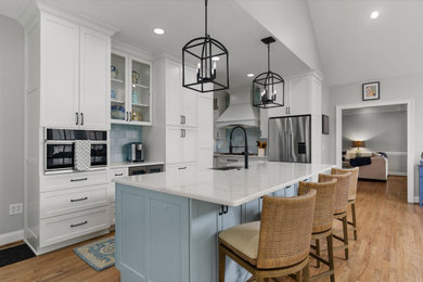 Kitchen - mid-sized coastal l-shaped medium tone wood floor and brown floor kitchen idea in Other with shaker cabinets, white cabinets, blue backsplash, ceramic backsplash, stainless steel appliances, an island, white countertops and quartz countertops