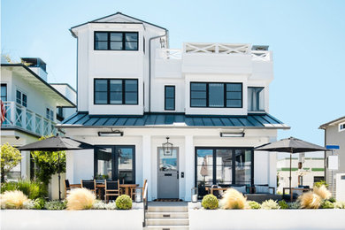 Photo of a large beach style two-storey white house exterior in Orange County with mixed siding, a gable roof and a metal roof.