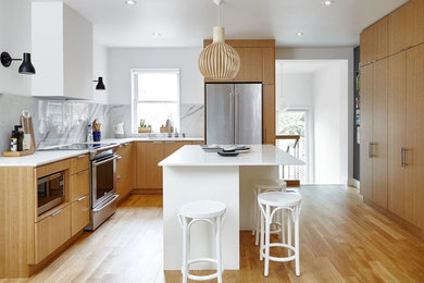 Design ideas for a scandinavian l-shaped open plan kitchen in Toronto with flat-panel cabinets, grey splashback, stainless steel appliances, with island, beige floor, an undermount sink, light wood cabinets, solid surface benchtops, marble splashback, light hardwood floors and white benchtop.