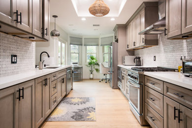 Example of a mid-sized transitional galley light wood floor enclosed kitchen design in Los Angeles with an undermount sink, recessed-panel cabinets, medium tone wood cabinets, white backsplash, stainless steel appliances, no island and white countertops