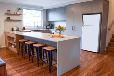 Large contemporary u-shaped separate kitchen in Melbourne with a double-bowl sink, flat-panel cabinets, grey cabinets, quartz benchtops, grey splashback, porcelain splashback, stainless steel appliances, medium hardwood floors, a peninsula, brown floor and grey benchtop.