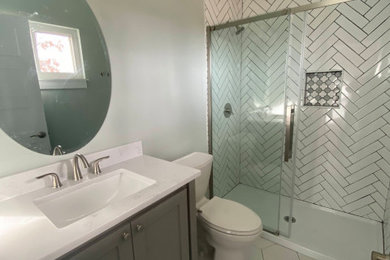 他の地域にある中くらいなコンテンポラリースタイルのおしゃれなバスルーム (浴槽なし) (インセット扉のキャビネット、グレーのキャビネット、アルコーブ型シャワー、分離型トイレ、白いタイル、セラミックタイル、白い壁、セラミックタイルの床、一体型シンク、珪岩の洗面台、白い床、引戸のシャワー、白い洗面カウンター、洗面台1つ、造り付け洗面台、クロスの天井、壁紙) の写真