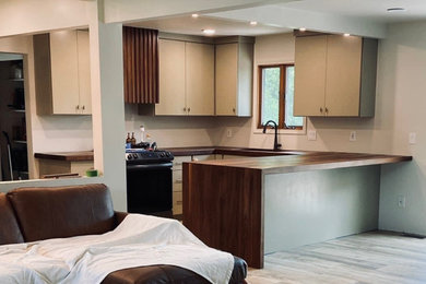 Example of a mid-sized minimalist u-shaped eat-in kitchen design in Los Angeles with flat-panel cabinets, beige cabinets, wood countertops, a peninsula and brown countertops