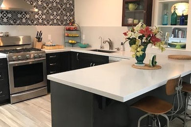 Inspiration for a mid-sized contemporary u-shaped light wood floor and beige floor eat-in kitchen remodel in San Diego with a drop-in sink, flat-panel cabinets, dark wood cabinets, solid surface countertops, black backsplash, ceramic backsplash, stainless steel appliances and a peninsula