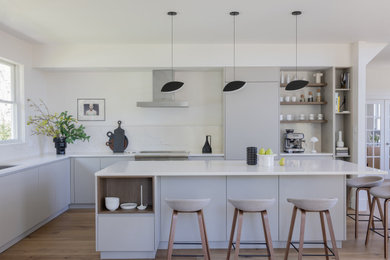 Eat-in kitchen - large modern l-shaped light wood floor eat-in kitchen idea in Boston with an undermount sink, flat-panel cabinets, gray cabinets, quartz countertops, white backsplash, quartz backsplash, stainless steel appliances, an island and white countertops