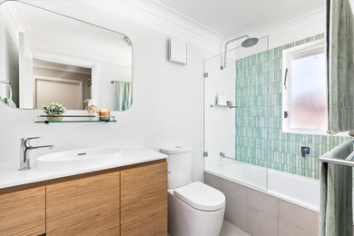 Photo of a mid-sized modern kids bathroom in Sydney with flat-panel cabinets, light wood cabinets, a drop-in tub, a shower/bathtub combo, a two-piece toilet, white tile, a vessel sink, solid surface benchtops, grey floor, an open shower, white benchtops, a single vanity and a freestanding vanity.