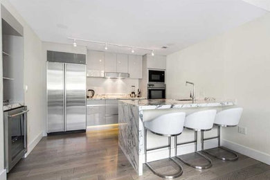 Open concept kitchen - mid-sized contemporary medium tone wood floor open concept kitchen idea in Miami with an undermount sink, flat-panel cabinets, white cabinets, white backsplash, stainless steel appliances, a peninsula and marble countertops