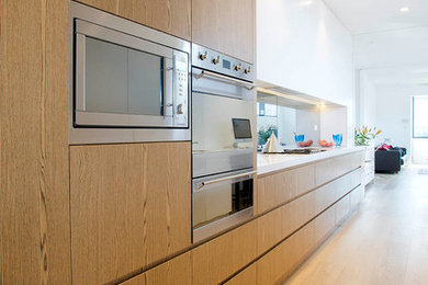 Large contemporary galley kitchen pantry in Sydney with a drop-in sink, solid surface benchtops, mirror splashback, stainless steel appliances, medium hardwood floors and no island.