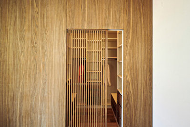 Diseño de vestidor unisex moderno de tamaño medio con armarios con puertas mallorquinas, puertas de armario de madera oscura y suelo de madera en tonos medios