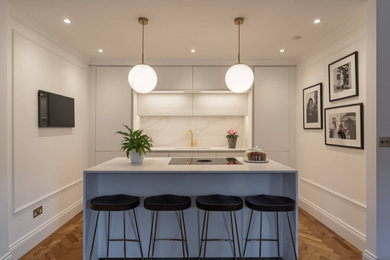 Inspiration for a medium sized contemporary single-wall open plan kitchen in Oxfordshire with a single-bowl sink, flat-panel cabinets, white cabinets, quartz worktops, white splashback, integrated appliances, medium hardwood flooring, an island, brown floors and white worktops.