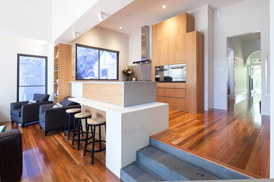 Design ideas for a contemporary u-shaped open plan kitchen in Melbourne with flat-panel cabinets, light wood cabinets, grey splashback, stone tile splashback, black appliances, medium hardwood floors, no island and brown floor.