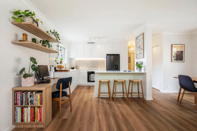 Small contemporary l-shaped open plan kitchen in Sydney with flat-panel cabinets, white cabinets, quartz benchtops, ceramic splashback, stainless steel appliances, medium hardwood floors, with island, brown floor, white benchtop and beige splashback.