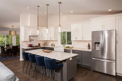 Inspiration for a country l-shaped medium tone wood floor and brown floor open concept kitchen remodel in Seattle with a farmhouse sink, shaker cabinets, white cabinets, quartz countertops, white backsplash, porcelain backsplash, stainless steel appliances, an island and white countertops
