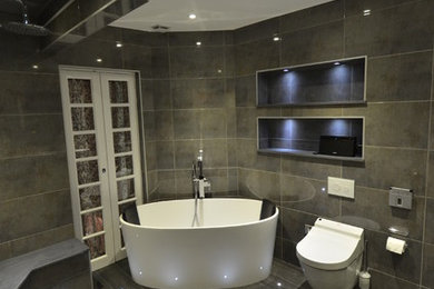 This is an example of a mid-sized contemporary wet room bathroom in London with furniture-like cabinets, black cabinets, a freestanding tub, a wall-mount toilet, gray tile, ceramic tile, with a sauna, a drop-in sink and granite benchtops.