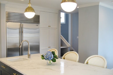 Kitchen - mid-sized transitional l-shaped kitchen idea in New York with quartz countertops, stainless steel appliances, an island, shaker cabinets and white cabinets