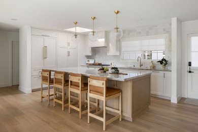 Mid-sized transitional light wood floor eat-in kitchen photo in Orange County with a drop-in sink, shaker cabinets, white cabinets, white backsplash, paneled appliances and an island