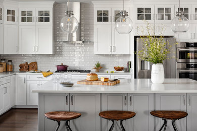 Inspiration for a large country l-shaped eat-in kitchen in DC Metro with a farmhouse sink, white cabinets, quartz benchtops, white splashback, subway tile splashback, stainless steel appliances, dark hardwood floors, with island, brown floor, white benchtop and shaker cabinets.
