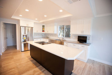 Inspiration for a mid-sized transitional l-shaped light wood floor eat-in kitchen remodel in Los Angeles with a farmhouse sink, white cabinets, granite countertops, gray backsplash, mosaic tile backsplash, stainless steel appliances, an island and recessed-panel cabinets