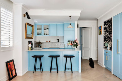 Photo of a small eclectic u-shaped open plan kitchen in Sydney with a farmhouse sink, shaker cabinets, blue cabinets, quartz benchtops, white splashback, ceramic splashback, black appliances, laminate floors, no island and white benchtop.