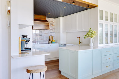 Design ideas for a small country u-shaped open plan kitchen in Other with a farmhouse sink, shaker cabinets, white cabinets, solid surface benchtops, white splashback, stone slab splashback, stainless steel appliances, medium hardwood floors, no island, brown floor, white benchtop and timber.
