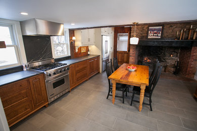 Mid-sized country l-shaped eat-in kitchen in Philadelphia with a farmhouse sink, soapstone benchtops, stone slab splashback, stainless steel appliances, porcelain floors and no island.