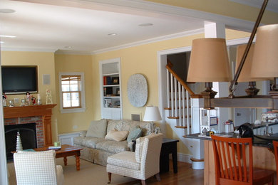 Example of a large classic medium tone wood floor living room design in New York with yellow walls, a standard fireplace, a wood fireplace surround and a wall-mounted tv