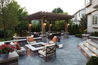 Example of a large minimalist front yard stone patio design in Cleveland with a fire pit and a pergola