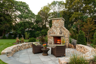 This is an example of a traditional backyard patio in Boston with a fire feature and natural stone pavers.