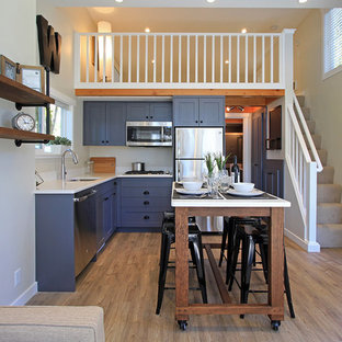 Свежая идея для дизайна: маленькая угловая кухня-гостиная в стиле кантри с врезной раковиной, фасадами в стиле шейкер, синими фасадами, столешницей из кварцевого композита, белым фартуком, техникой из нержавеющей стали, полом из винила и островом - отличное фото интерьера