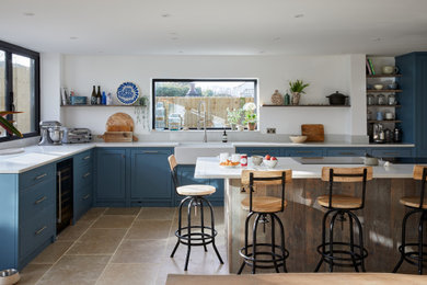 Inspiration for a large modern l-shaped open plan kitchen in London with a belfast sink, shaker cabinets, blue cabinets, quartz worktops, white splashback, window splashback, integrated appliances, ceramic flooring, an island, brown floors and white worktops.