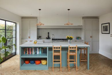 Inspiration for a medium sized traditional single-wall kitchen/diner in London with a submerged sink, shaker cabinets, green cabinets, quartz worktops, engineered quartz splashback, stainless steel appliances, medium hardwood flooring, an island, white worktops and a chimney breast.