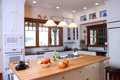 Large arts and crafts l-shaped light wood floor kitchen photo in Other with a farmhouse sink, shaker cabinets, white cabinets, white backsplash, ceramic backsplash, white appliances and an island