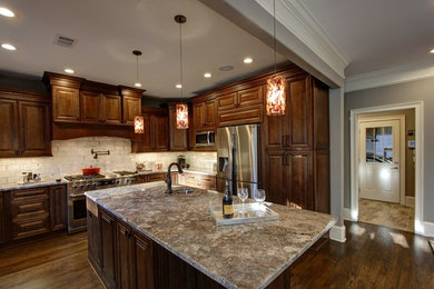 Inspiration for a mid-sized timeless u-shaped medium tone wood floor and brown floor kitchen remodel in Atlanta with an undermount sink, raised-panel cabinets, dark wood cabinets, granite countertops, beige backsplash, brick backsplash, stainless steel appliances and an island