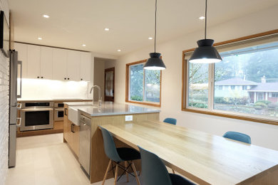 Eat-in kitchen - small mid-century modern porcelain tile and beige floor eat-in kitchen idea in Portland with a farmhouse sink, flat-panel cabinets, white cabinets, quartzite countertops, white backsplash, stainless steel appliances, an island and gray countertops