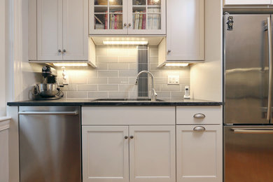 Small transitional galley medium tone wood floor enclosed kitchen photo in Boston with an undermount sink, shaker cabinets, white cabinets, granite countertops, gray backsplash, subway tile backsplash, stainless steel appliances and an island