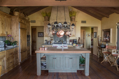 Inspiration for a large rustic u-shaped dark wood floor and brown floor eat-in kitchen remodel in Santa Barbara with a farmhouse sink, recessed-panel cabinets, distressed cabinets, wood countertops, paneled appliances, an island and brown countertops