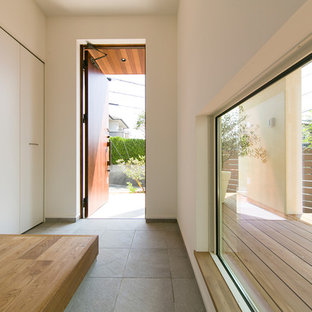 他の地域の片開きドアアジアンスタイルのおしゃれな玄関ホール (白い壁、木目調のドア、グレーの床) の写真
