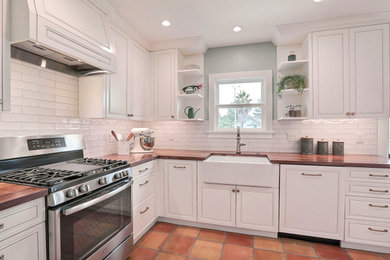 Example of a large farmhouse terra-cotta tile and orange floor kitchen design in San Francisco with a farmhouse sink, shaker cabinets, white cabinets, wood countertops, white backsplash, subway tile backsplash, stainless steel appliances and brown countertops